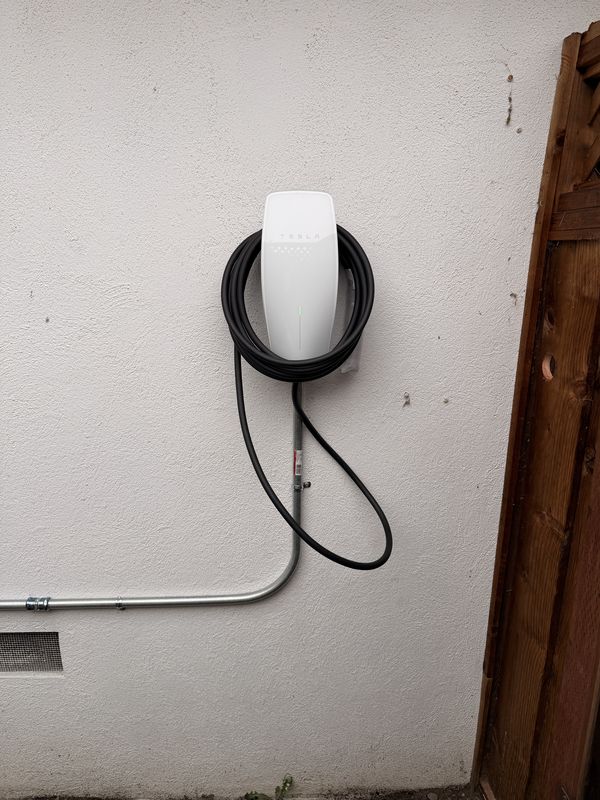 Tesla Wall Connector with coiled charge cable on a stucco wall