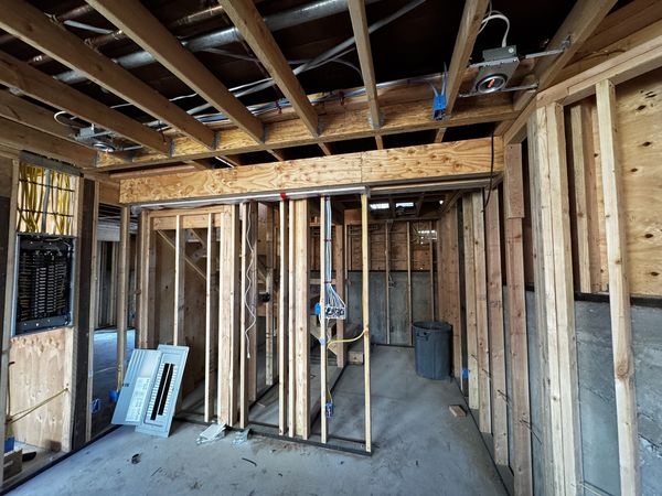 Open framing with new branch circuits routed overhead and load centers staged during rough-in
