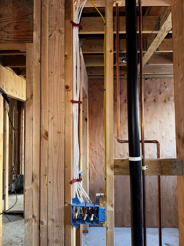 Home-run cables trained down a stud into a junction box beside plumbing risers